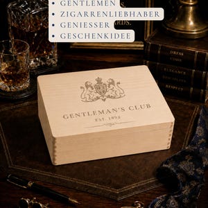 Peut inclure: Une bo&icirc;te rectangulaire en bois clair avec un couvercle &agrave; charni&egrave;re pr&eacute;sentant un blason grav&eacute; au laser repr&eacute;sentant deux lions entourant un &eacute;cusson, le texte GENTLEMAN'S CLUB et le texte EST. 1892 avec une fioriture d&eacute;corative centr&eacute;e.