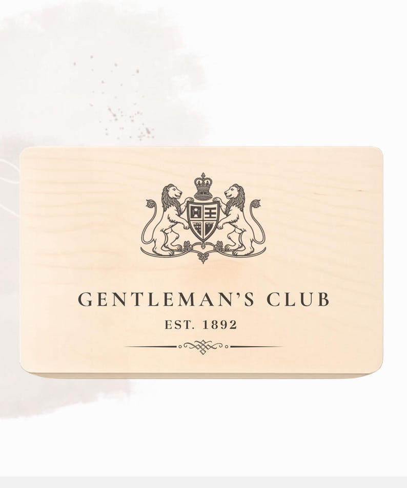 Peut inclure: Une bo&icirc;te rectangulaire en bois clair pr&eacute;sentant un motif imprim&eacute; marron fonc&eacute; compos&eacute; de deux lions entourant un blason central surmont&eacute; d'une couronne. Sous l'embl&egrave;me, le texte indique GENTLEMAN'S CLUB, EST. 1892, avec une ligne d&eacute;corative.