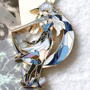 Może przedstawiać: Szczegółowa emaliowana przypinka przedstawiająca postać w stylu anime z białymi włosami i niebieskim strojem, trzymającą miecz. Przypinka osadzona jest na złotym księżycu w kształcie półksiężyca i kryształowej podstawie, z odcieniami niebieskiego i czarnego.