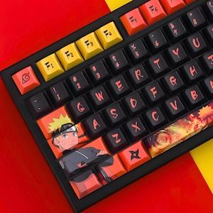 May include: Black mechanical keyboard with custom keycaps featuring a Naruto theme. The keycaps are black, orange, and yellow, with character art and symbols. The keyboard has a red and yellow background.