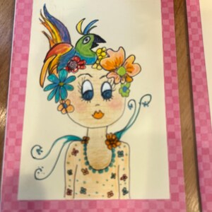 Pode incluir: Ilustração fantasiosa de uma menina adornada com flores e um adorno de cabeça de pássaro colorido. A obra de arte apresenta um fundo de pêssego claro com uma borda rosa quadriculada. O vestido da menina é amarelo claro com pequenos padrões florais.