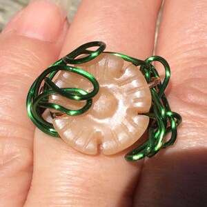 May include: A ring made with green wire wrapped around a round, light brown button.