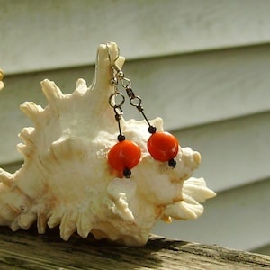May include: A pair of dangle earrings with orange glass beads and black spacer beads hanging from silver-toned ear wires.