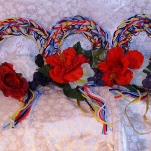 以下が含まれることがあります： 赤、白、青、黄色の糸で編まれた花輪が3つ、赤、白、紫の花で飾られています。