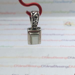 May include: A silver pendant with a square white stone set in a silver frame. The pendant has intricate silver detailing around the stone and a loop at the top for attaching to a chain.