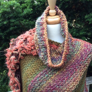 Puede incluir: Una bufanda de punto multicolor con un borde rizado. La bufanda está hecha de un hilo suave y texturizado y presenta una variedad de colores, incluyendo verde, marrón, rojo y morado.