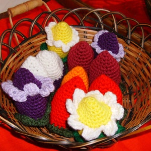 Op de afbeelding: Een mand gevuld met gehaakte bloemvormige ornamenten. De ornamenten zijn in verschillende kleuren, waaronder paars, rood, geel en wit.