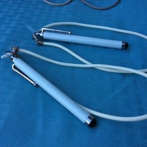 May include: Two white stylus pens with a white cord attached to each. The pens have a silver clip and a silver tip.