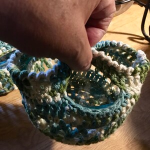 Könnte beinhalten: Eine gehäkelte Einmachglas-Abdeckung in Grün, Weiß und Blau. Die Abdeckung ist mit einem einfachen Stichmuster gearbeitet und hat einen gewellten Rand.