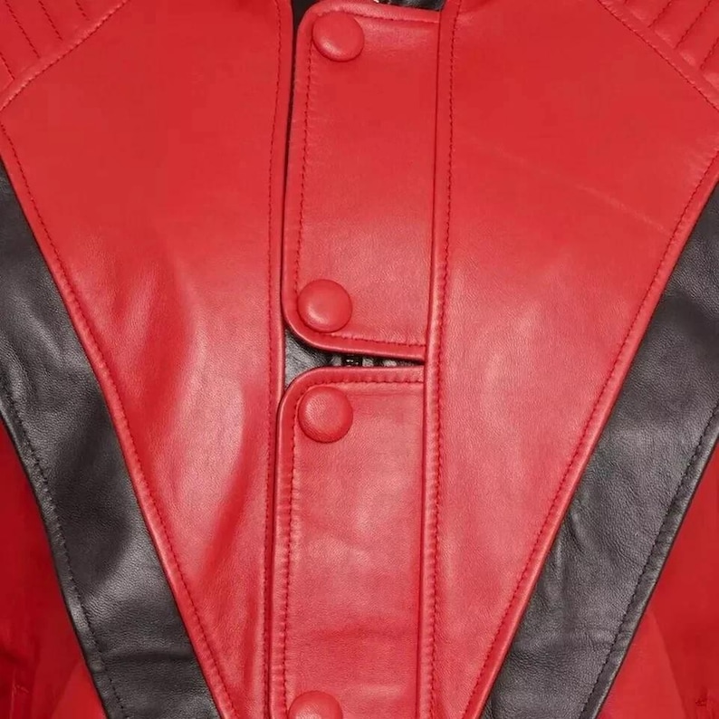 May include: Close-up of a red leather jacket with black detailing. The jacket has a button-up front and a unique design with black panels. The stitching is visible, emphasising the tailored construction of the garment.
