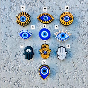 Puede incluir: Una colección de diez amuletos decorativos con diseños de ojo turco y mano de Fátima. Los amuletos tienen varias formas y colores, incluyendo azul, amarillo, negro y blanco. Estos amuletos probablemente están destinados a zapatos u otros accesorios.