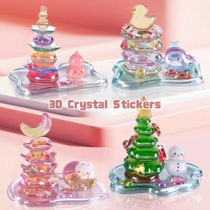 Op de afbeelding: Vier sets 3D kristallen stickers. Elke set bevat een stapel kleurrijke, transparante vormen, bekroond met een eend, een halve maan of een kerstboom. Elke set bevat een klein, decoratief beeldje op een heldere, golvende basis. De tekst "3D Crystal Stickers" is zichtbaar.