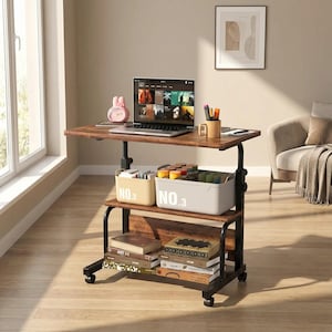 May include: A brown, adjustable height desk with a black metal frame. The desk has two shelves, one holding books and the other with storage bins. A laptop, alarm clock, and pens sit on the top shelf. The desk is on wheels.
