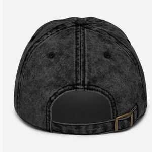 May include: A black, distressed baseball cap with a curved peak. The cap has a metal buckle at the back for size adjustment. The fabric has a faded, vintage look.