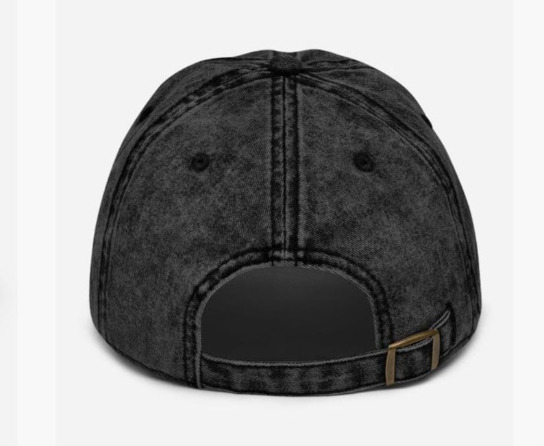 May include: A black, distressed baseball cap with a curved peak. The cap has a metal buckle at the back for size adjustment. The fabric has a faded, vintage look.