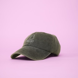Könnte beinhalten: Olivgrüne Baseballkappe mit gebogenem Schirm. Auf der Kappe ist das Wort "FIGGO" in Weiß gestickt, zusammen mit einer kleinen Grafik. Der Hut ist vor einem rosa Hintergrund platziert.