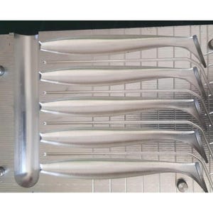 Może przedstawiać: Zbliżenie metalowej formy do przynęt wędkarskich. Forma jest srebrna i zawiera sześć srebrnych przynęt. Przynęty mają opływowy kształt z zakrzywionym ogonem. Forma znajduje się na metalowej powierzchni.