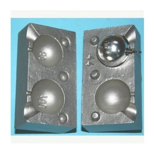 May include: Two-part metal fishing sinker mould. The grey mould has cavities for creating round sinkers. One side has a sinker in place. The mould is designed to create 98 and 100-ounce sinkers.