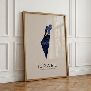 Könnte beinhalten: Gerahmter Kunstdruck mit einer abstrakten Karte Israels in Marineblau und Gold auf beigem Hintergrund. Das Wort "ISRAEL" ist in Schwarz unter der Karte gedruckt, zusammen mit den Koordinaten 31° 46' N 35° 13' E.
