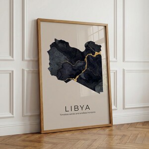Puede incluir: Lámina artística enmarcada con un mapa estilizado de Libia en azul oscuro y dorado sobre un fondo beige. La palabra "LIBIA" está impresa debajo del mapa, con la frase "Arenas atemporales y horizontes infinitos" debajo.