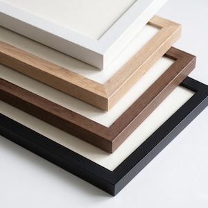 Könnte beinhalten: Ein Stapel von vier Bilderrahmen in verschiedenen Farben: Weiß, helles Holz, mittelbraun und Schwarz. Jeder Rahmen hat ein weißes Passepartout und ein schlichtes, modernes Design, geeignet für Kunstwerke oder Fotos.