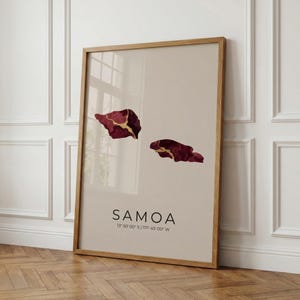 May include: A framed art print featuring a beige background with two abstract shapes in burgundy and gold. The word "SAMOA" is printed in black, along with coordinates. The frame is made of light brown wood.