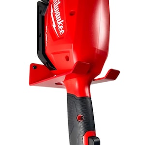 May include: A red Milwaukee FUEL power tool with a black handle and a metal wall mount. The tool is hanging on the wall mount.