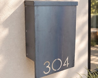 May include: A rectangular, dark grey metal wall-mounted post box featuring a flat top lid and a vertical front panel. The number 304 is cut out from the bottom right corner of the front panel, revealing a lighter metallic colour through the stencil.