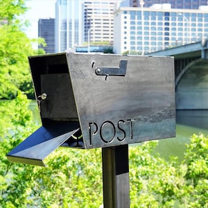 May include: A gray metal mailbox with a flap that opens for mail delivery. The mailbox is mounted on a black metal pole and has the word "POST" cut out on the front.
