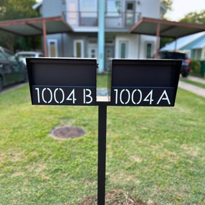 May include: Two black metal mailboxes with white numbers and letters. The mailbox on the left says "1004 B" and the mailbox on the right says "1004 A".