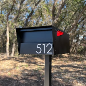 May include: Black mailbox with a red flag and the number 512 on the front. The mailbox is mounted on a black metal post.