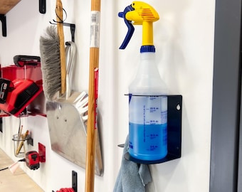 Puede incluir: Un soporte de pared de metal negro para botella de spray con una botella de spray azul llena de líquido azul. Un paño de limpieza azul cuelga del soporte.