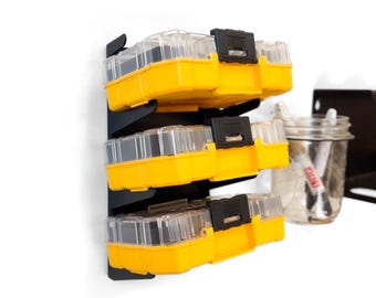 Puede incluir: Tres cajas de almacenamiento de plástico amarillo y negro con tapas transparentes están apiladas en un organizador de pared negro. Las cajas están etiquetadas con "DEWALT".