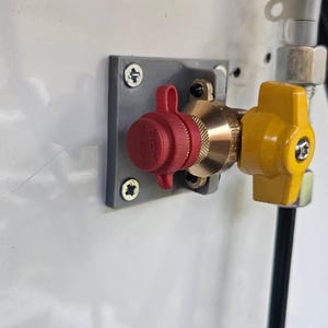 Può includere: Un primo piano di un gruppo valvola del gas. Presenta un tappo rosso, raccordi in ottone e una maniglia gialla. Il gruppo è montato su una superficie bianca con una staffa grigia e tubi neri.