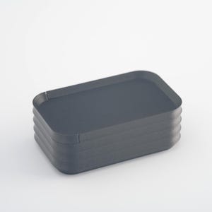 May include: A stack of four dark gray rectangular trays with rounded corners. The trays are stacked on top of each other, creating a layered effect. The trays are made of a matte material and are set against a white background.
