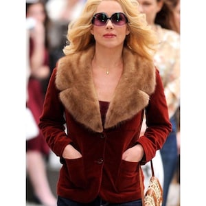 Op de afbeelding: Een bordeauxrode fluwelen blazer met een bruine bontkraag. De blazer heeft twee voorzakken en een enkele knoopsluiting. De persoon draagt een zonnebril en een gouden ketting.
