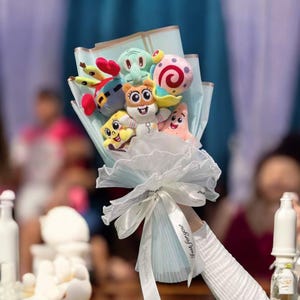Op de afbeelding: Een boeket van pluche cartoonkarakters, waaronder SpongeBob SquarePants en Patrick Star, verpakt in lichtblauw papier en vastgebonden met een wit lint. Op het lint staat de tekst "Just for you".