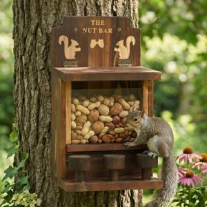 Può includere: Un alimentatore per scoiattoli in legno con la scritta "THE NUT BAR" e sagome di scoiattoli. L'alimentatore è pieno di varie noci e uno scoiattolo è appollaiato sulla parte anteriore. L'alimentatore è attaccato a un albero.