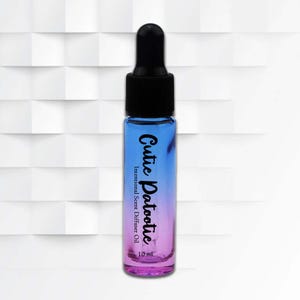 Może przedstawiać: Mała, gradientowa szklana butelka w kolorze niebieskim i fioletowym z czarnym zakraplaczem. Butelka jest oznaczona napisem "Cutie Patootie Intentional Scent Diffuser Oil" i zawiera 10 ml olejku. Tło to biały geometryczny wzór.