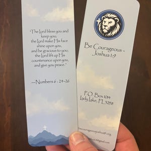 May include: Two rectangular bookmarks with a light blue sky background. One bookmark features a quote from Numbers 6:24-26. The other bookmark has a lion logo and the text "Be Courageous - Joshua 1:9".