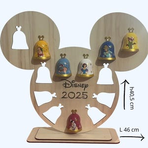 Op de afbeelding: Houten Disney-display, gevormd als Mickey Mouse oren, met klokvormige ornamenten. Het display is 46 cm breed en 40,5 cm hoog. De ornamenten tonen Disney-personages. De tekst "Disney 2025" is op het display gedrukt.
