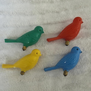 Może przedstawiać: Cztery kolorowe żarówki w kształcie ptaków. Ptaki są zielone, czerwone, żółte i niebieskie. Każdy ptak ma podstawę żarówki ułatwiającą mocowanie do łańcucha świetlnego. Idealne do dekoracji świątecznych.