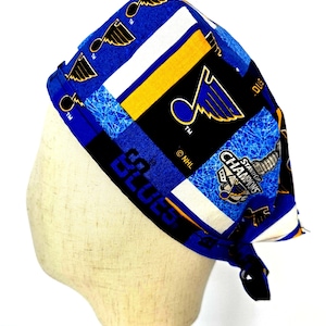 May include: A blue, black, and white patterned head covering featuring the St. Louis Blues logo and the words "Stanley Cup Champions." The head covering is tied at the back and is displayed on a mannequin head.