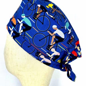 May include: A blue surgical scrub cap featuring a repeating pattern of cyclists on bicycles. The cyclists are depicted in various colors, including white, black, and yellow, against a blue background. The cap is tied at the back.