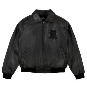 May include: Black leather bomber jacket with a zip-up front, collar, and ribbed cuffs and hem. Features a small emblem on the chest and the brand name "AVIREX" on the collar.