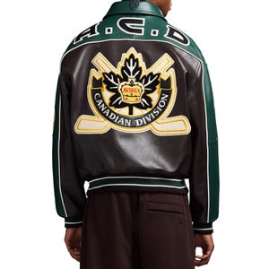 Puede incluir: Una chaqueta de cuero marrón y verde con ribetes blancos y cuello negro. La parte trasera de la chaqueta presenta un gran emblema con el texto "CANADIAN DIVISION" y un diseño de hoja de arce. La chaqueta tiene el texto "A.C.D." en el cuello.