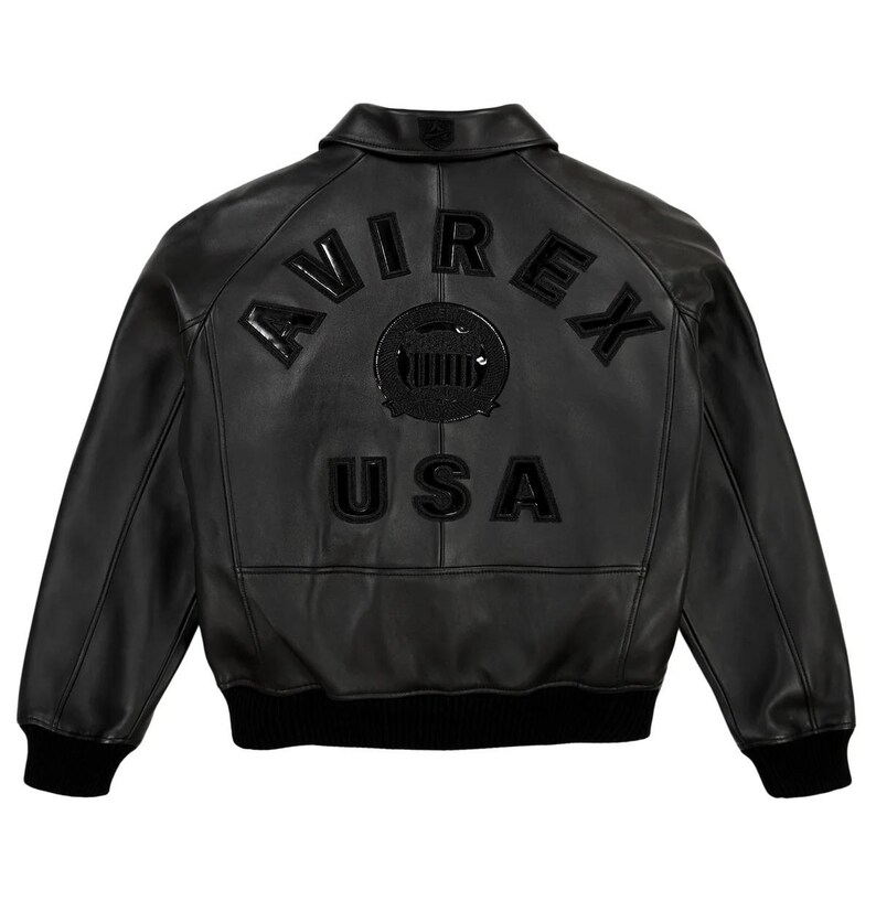 May include: Black leather jacket with the word "AVIREX" arched across the upper back, above a circular emblem and the word "USA". The jacket has a ribbed hem and cuffs, and a classic collar.