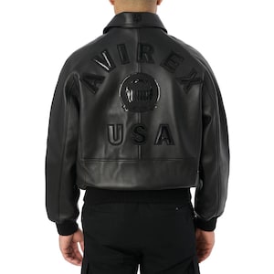May include: Black leather bomber jacket with the word "AVIREX" and "USA" stitched on the back. The jacket has a ribbed hem and cuffs, a collar, and a zip closure. The jacket is a classic style.