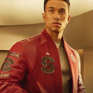 May include: A deep red varsity-style jacket featuring a large black letter S on the chest, a smaller Mir logo above it, and a circular patch on the right sleeve with the text LICA and AM surrounding a stylized graphic of a bird-like creature.