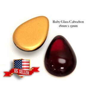 May include: Two teardrop-shaped cabochons. One is a solid gold color, the other is a deep ruby red. The text reads "Ruby Glass Cabochon 18mm x 13mm". A "US Seller" ribbon and American flag are in the lower left.